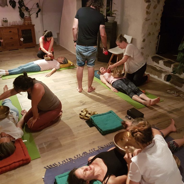 Pratique en binôme lors d’une formation au bol tibétain Participants en formation s’exerçant au soin sonore en binômes, posant les bols tibétains sur les corps allongés.